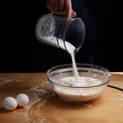 Woman hand pouring sugar into a bowl filled with dough on a wood