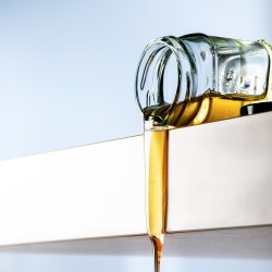 Honey flows from a tipped glass jar over the table edge, light b
