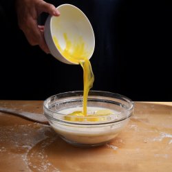 Woman hand pouring egg into a bowl filled with flour and milk on